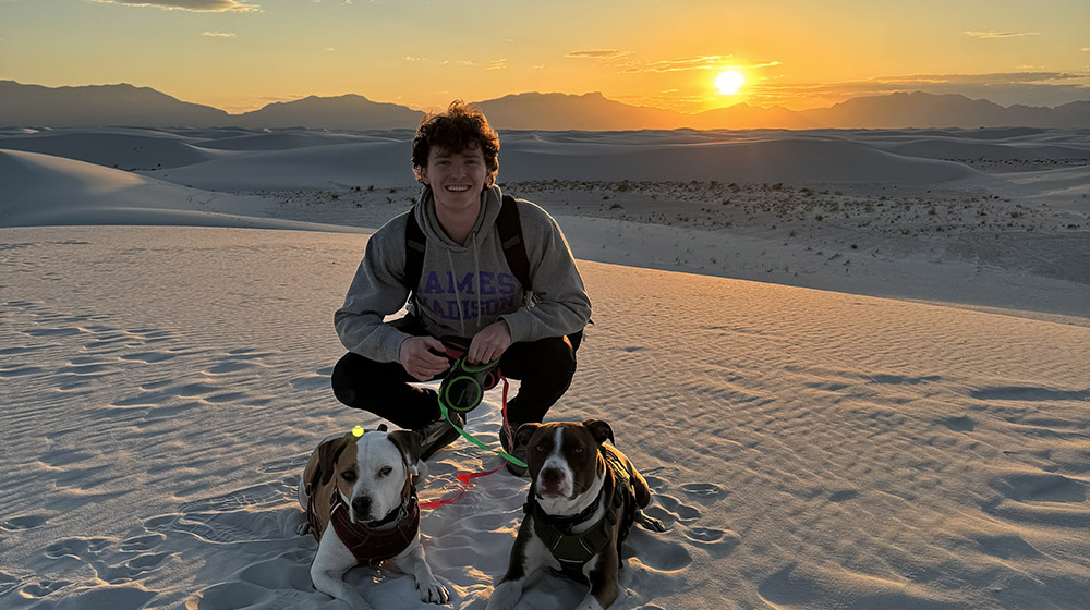 Henry Neri outside with two dogs with the setting sun behind him